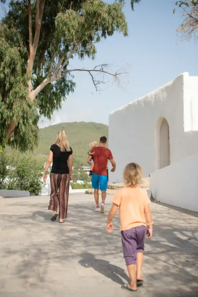 Gezin wandelt samen buiten op Ibiza, ouders met kinderen richting witte huizen en natuur, symbool voor vrijheid en samen op pad zijn