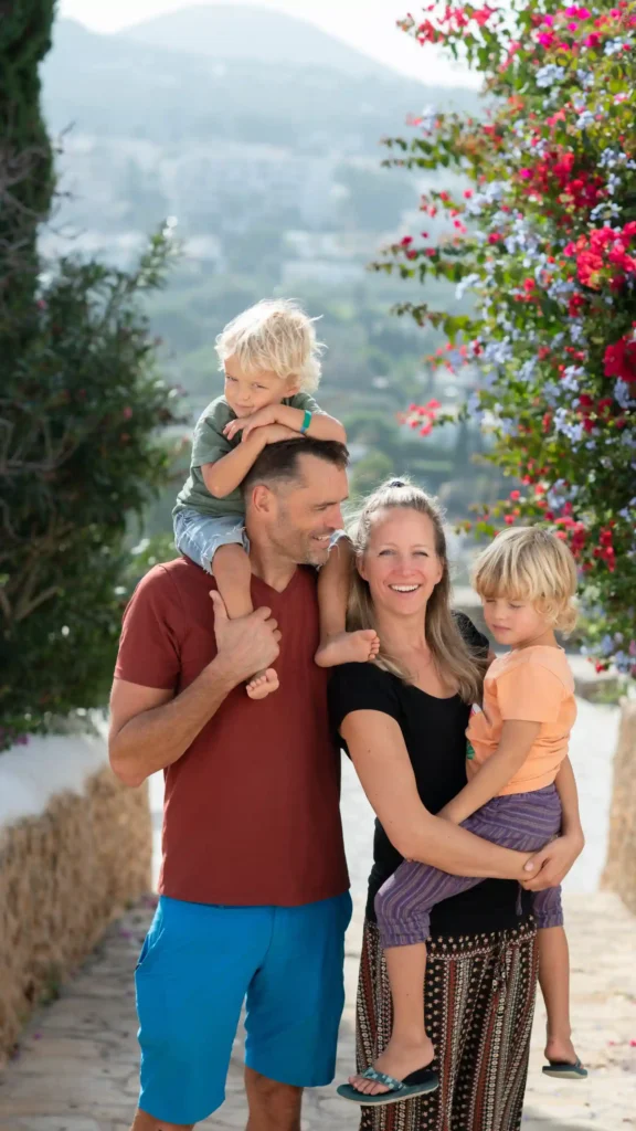 Gezin van de Paperclip Tribe lachend op een zonnig bloemenpad in Zuid-Spanje – samen op weg naar een vrijer leven buiten het systeem.